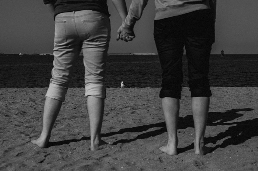 detail of the legs and holding hands, a seagull on the beach