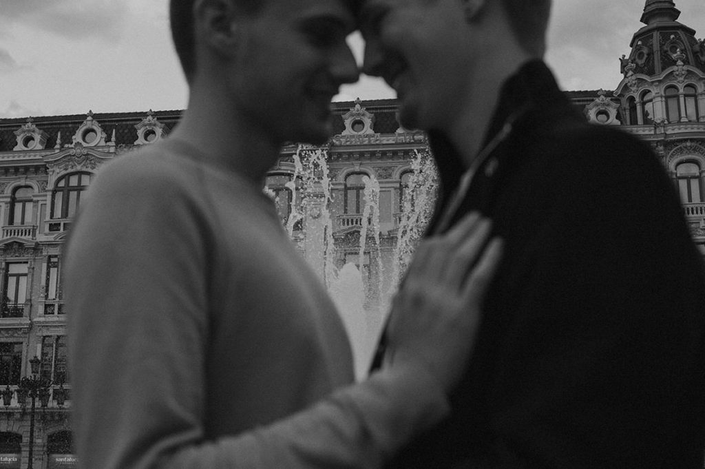 Gay couple cuddling in Oviedo, with a fountain in the background
